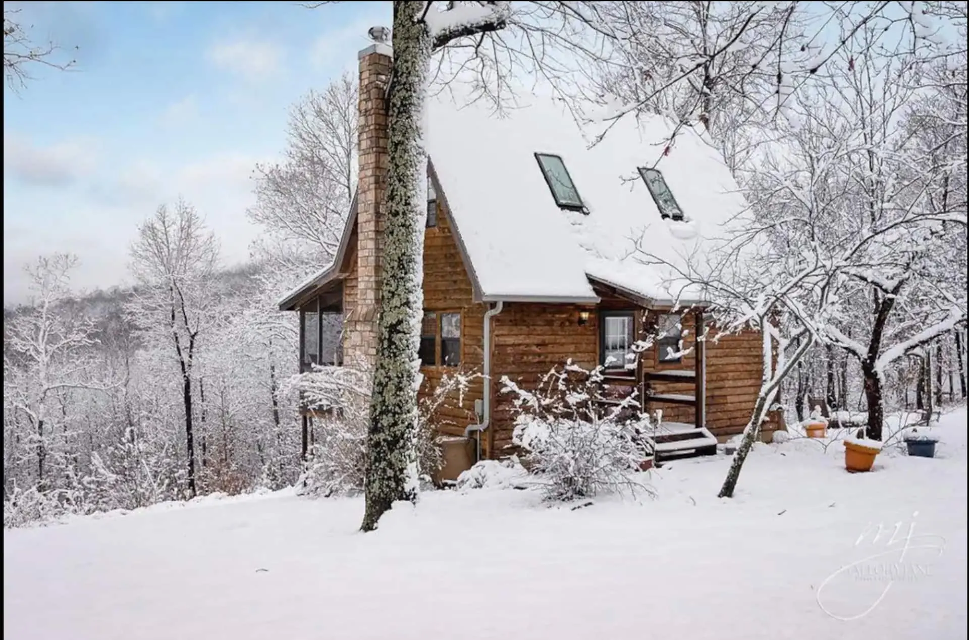 A Still Point Cabin under fresh snow in winter, stone chimney rising through bare Ozark hardwoods